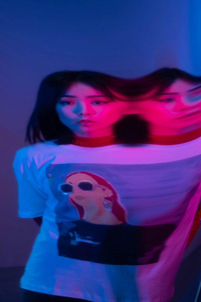 pexels photo 6491663 6491663 Artistic portrait of a woman wearing a graphic tee under a colorful light with prism distortion.